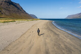 Girl walking alone on sandy beach close to Önundarfjörður Pier in Westfjords, Iceland. Beautiful nature and travel destination 