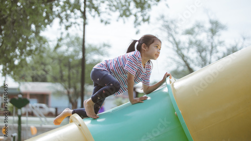 Little Asian girl playing on slide at the playground in the park.