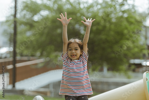 Little Asian girl playing on slide at the playground in the park.