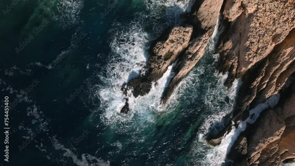 Aerial top down view of waves crashing on a rocky shore with sharp sea cliffs Aerial top down view of waves crashing on a rocky shore with sharp sea cliffs