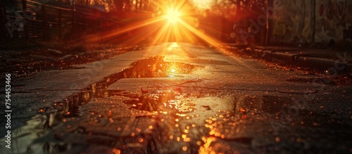 The suns rays illuminate a wet street  creating reflections on the glistening pavement.