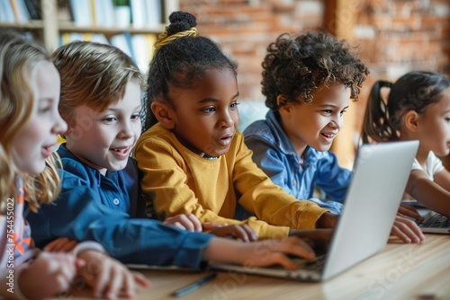A group of children are sitting around a table looking at a laptop. They are all smiling. Concept of fun and learning