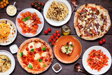 Delicious Italian food table scene. Selection of pizzas, pastas, gnocchi, risotto and bruschetta. Top view on a dark wood background.