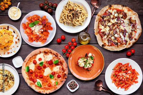 Delicious Italian food table scene. Selection of pizzas, pastas, gnocchi, risotto and bruschetta. Top view on a dark wood background.