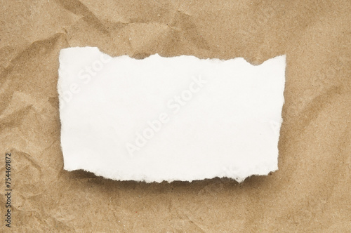 White paper  piece with ripped edge on brown paper background