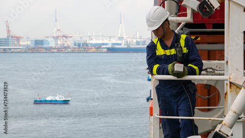 Seaman crew member of cargo vessel  equipped with personal protective equipment operate life boat davit  on the cargo ship in helmet with walkie talkie.