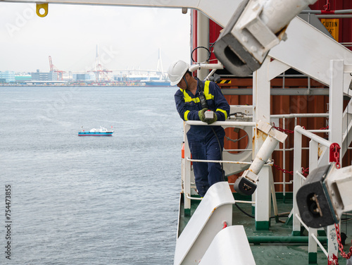 Seaman crew member of cargo vessel  equipped with personal protective equipment operate life boat davit  on the cargo ship in helmet with walkie talkie.