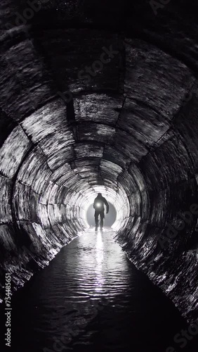 A man with a lantern walks in an underground round concrete rain collector.