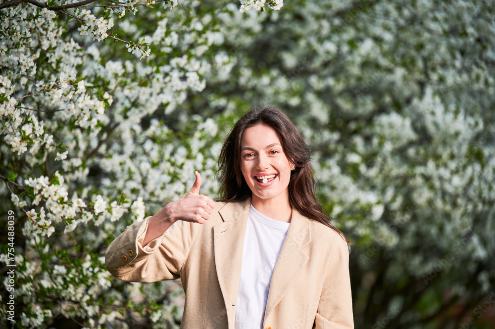 Woman allergic suffering from seasonal allergy at spring. Young happy woman applying allergy pill, giving thumbs up, posing in blossoming garden at springtime. Antihistamine medication concept Woman allergic suffering from seasonal allergy at spring. Young happy woman applying allergy pill, giving thumbs up, posing in blossoming garden at springtime. Antihistamine medication concept