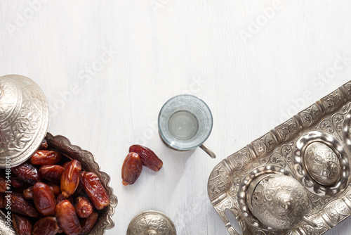 Top view on silver plate with date fruits and glass of water on a white wooden background. Ramadan background. Ramadan kareem.