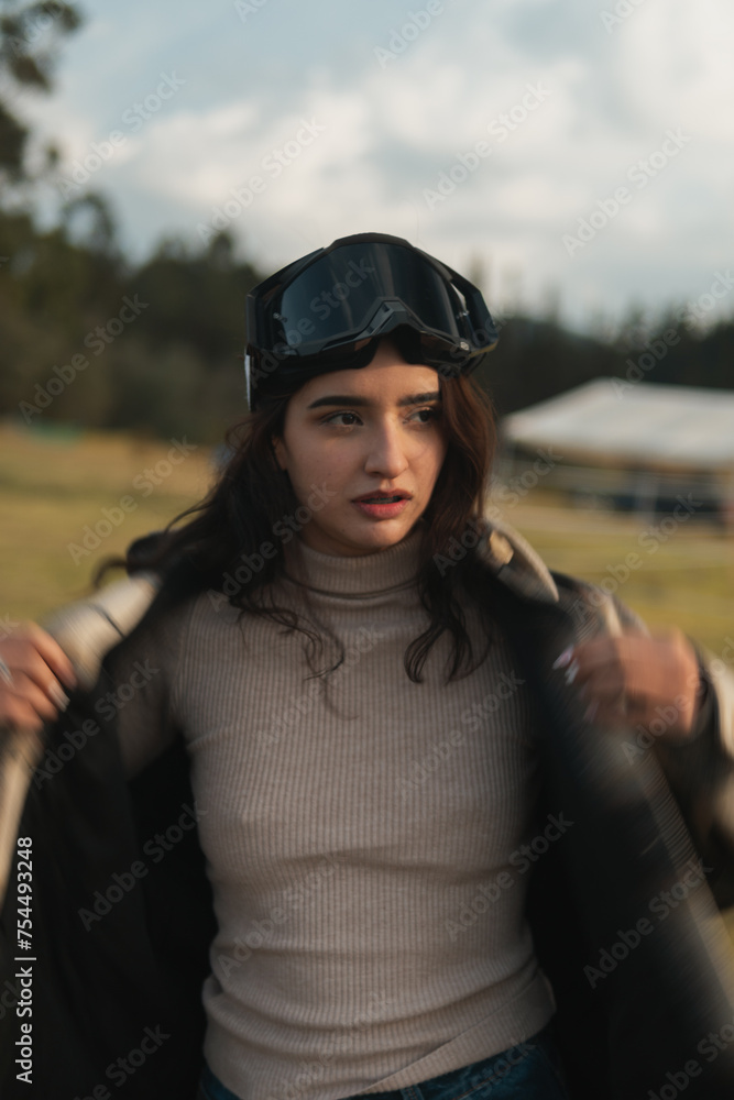 Close-up of a young woman donning motocross goggles, embodying an adventurous spirit in an outdoor setting Close-up of a young woman donning motocross goggles, embodying an adventurous spirit in an outdoor setting