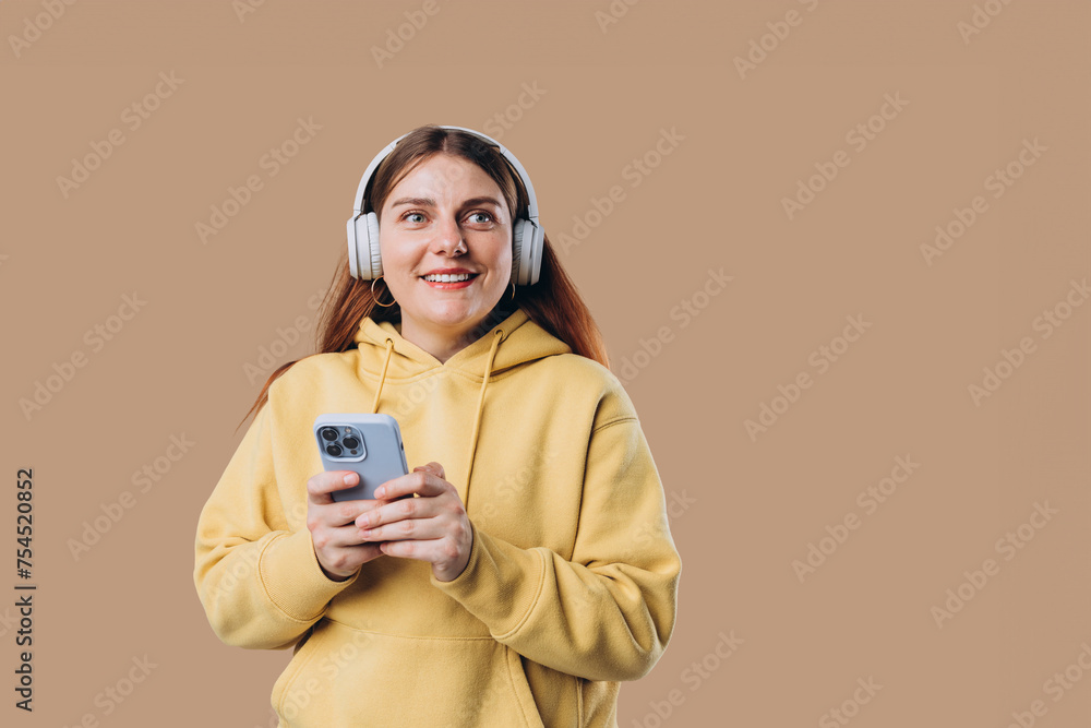 Beautiful young 30s woman wearing white wireless headphones and listening to music and using smart phone, girl isolated over colorful background wall