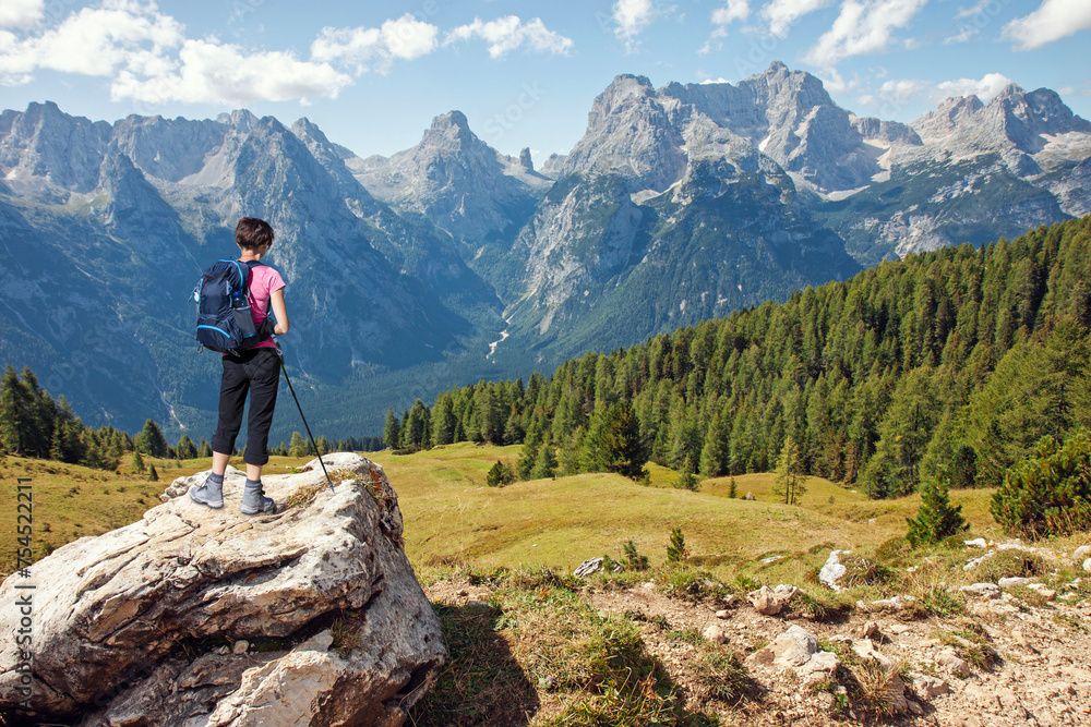 Fototapeta premium Woman hiker standing on stone rock and looking at scenic mountains in summer