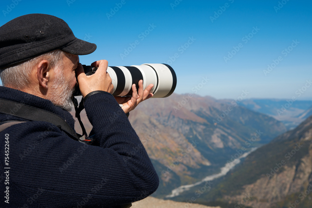 An adult man with a camera with a long-focus lens on the background of a high-mountainous picturesque landscape. Fragment. Close-up. Copy space.