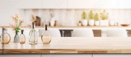 A wooden kitchen counter is covered with a variety of bottles holding aromatic sticks. The background features a blurred Scandinavian kitchen with white architecture and a dining table.