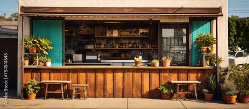 A small outdoor bar setup with various potted plants placed along the exterior. The bar is designed for customers to enjoy drinks and socialize in a casual outdoor setting. © Vusal