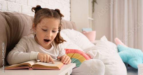 Cute little girl reading book in bedroom