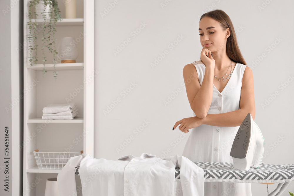 Thoughtful young woman looking at shirt on ironing board at home Thoughtful young woman looking at shirt on ironing board at home