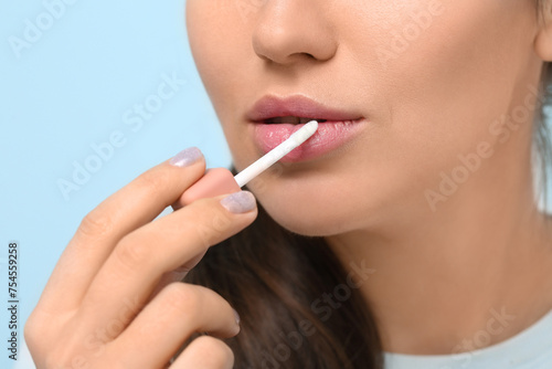 Young woman applying lipgloss on color background  closeup