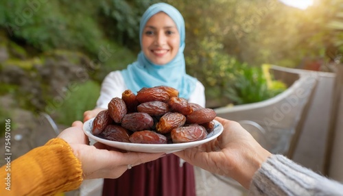 Concept Giving or Charity during Ramadhan Holy Month, Female Muslim Hand Over A Plate of Dates Fruit hurma to Other. Ifthar and Ramadan Kareem Concepts.