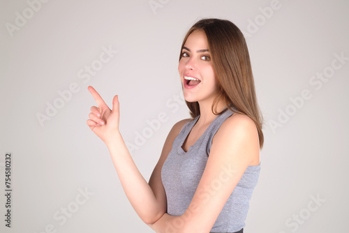 Beauty brunette woman gesturing with fingers, showing away. Young woman pointing copy space. Studio portrait of Girl looking at camera and pointing away on isolated background.