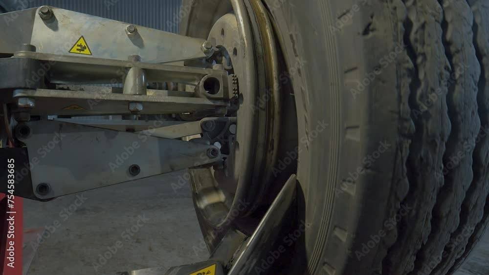 Heavy Machine Mechanism Slides Under Tire To Show Bare Wheel. Automated Heavy Machine Moves Tire For Maintenance. Checking Heavy Industrial Machine Tire Using Car Service Equipment. Close Up Heavy Machine Mechanism Slides Under Tire To Show Bare Wheel. Automated Heavy Machine Moves Tire For Maintenance. Checking Heavy Industrial Machine Tire Using Car Service Equipment. Close Up