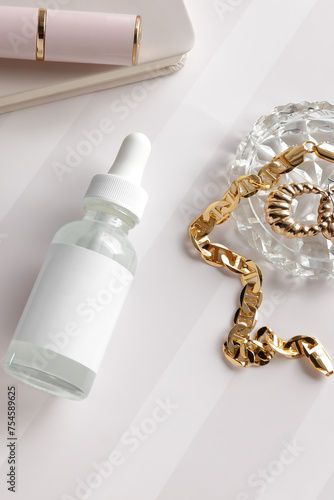 mockup of a clear white dropper essential oil bottle with crystal dish with gold jewelry, bracelet, earrings, lipstick and notebook in soft light