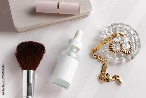 mockup of a white dropper bottle with blank white label, feminine styled with a cosmetic makeup brush, lipstick, crystal dish with gold jewelry, gold bracelet, gold earrings, and notebook