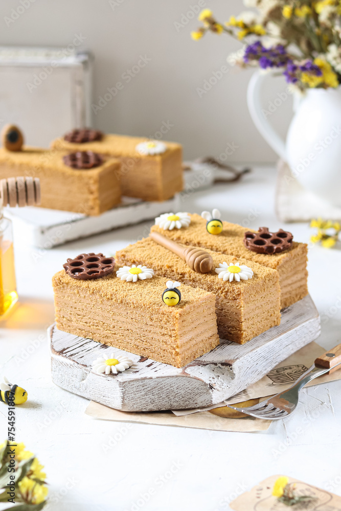 Honey layer cake with bee and daisy decorations on a rustic board.
