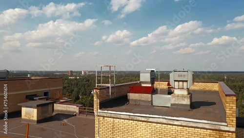 aerial photography. A quadcopter on a sunny summer day flies back from a multi-storey residential high-rise building behind which there is a large green field and forest.