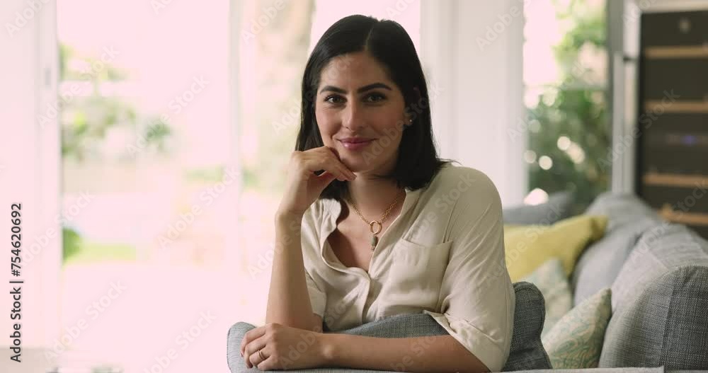 Attractive Mexican young woman homeowner posing for camera seated, relaxing on cozy couch in sunny living room, enjoy day-off, vacation in modern own or rented apartment. Happy female tenant portrait Attractive Mexican young woman homeowner posing for camera seated, relaxing on cozy couch in sunny living room, enjoy day-off, vacation in modern own or rented apartment. Happy female tenant portrait