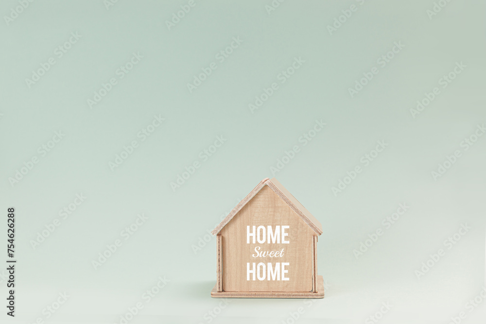 Simplistic wooden house model isolated on pale green background, with text Home Sweet Home on wall Simplistic wooden house model isolated on pale green background, with text Home Sweet Home on wall