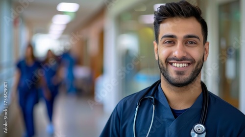 Smiling Middle Eastern man nurse with stethoscope looking at camera. Young doctor smiling while standing in hospital corridor with the health care team in the background. Successful Indian surgeon