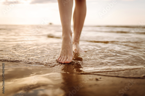 Close- up leg of young woman walking along wave of sea water and sand on the summer beach. Travel, weekend, relax and lifestyle concept.