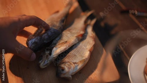 Close-up. Two salty dried cured fish lie on a wooden board. A man's hand places another stockfish on the board