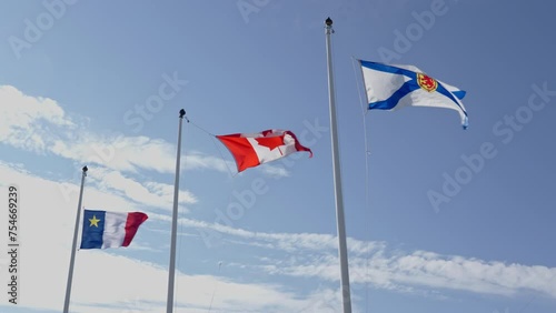 The Acadian flag, the Canadian flag and the Nova Scotia flag in a row and blowing in the wind, against a blue sky with clouds, on a windy summer day