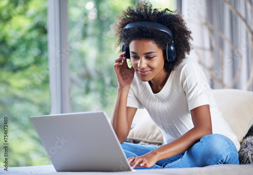 Black woman, headphones and laptop at home for online teaching, e learning and education in living room. Female person, scholar and university student in house for remote class, studying and tuition photo