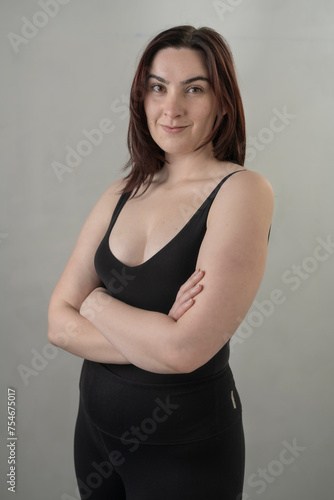 Young brunette womain in black tank top poses befoe a white wall in soft light photo