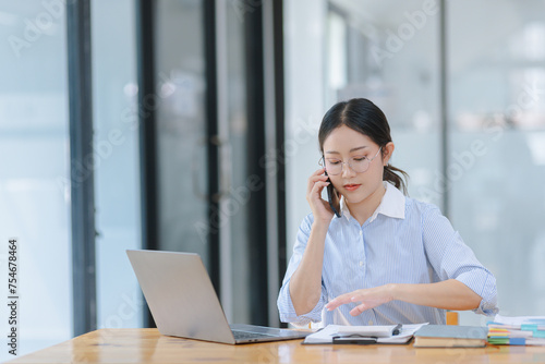 Asian accounting woman using smartphone working with document paper and laptop computer at table office, Financial and accounting woman concept. 