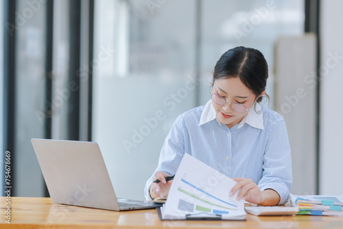 Asian accounting woman working with document paper and laptop computer at table office, Financial and accounting woman concept.  © SOMKID
