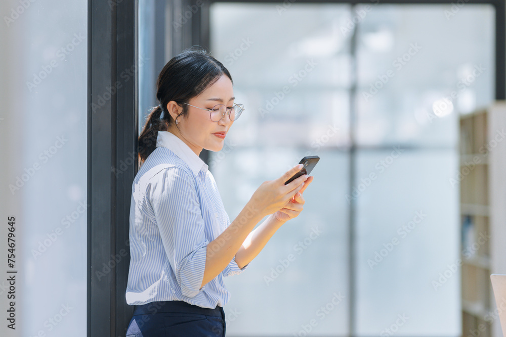 Asian businesswoman using smartphone standing at the office. 