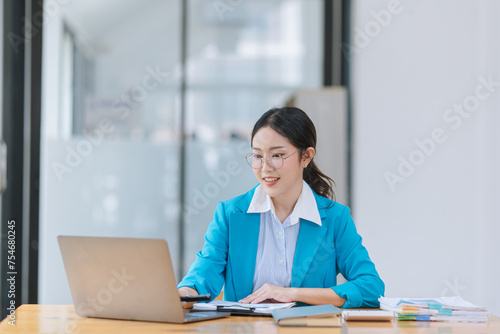 Asian businesswoman wear glasses with Wear a suit working on digital laptop computer in office.  © SOMKID