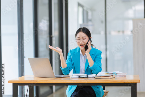 Asian businesswoman wearing a suit using smartphone with digital laptop computer working at modern office, Asian beautiful businesswoman in red suit working in the modern office.