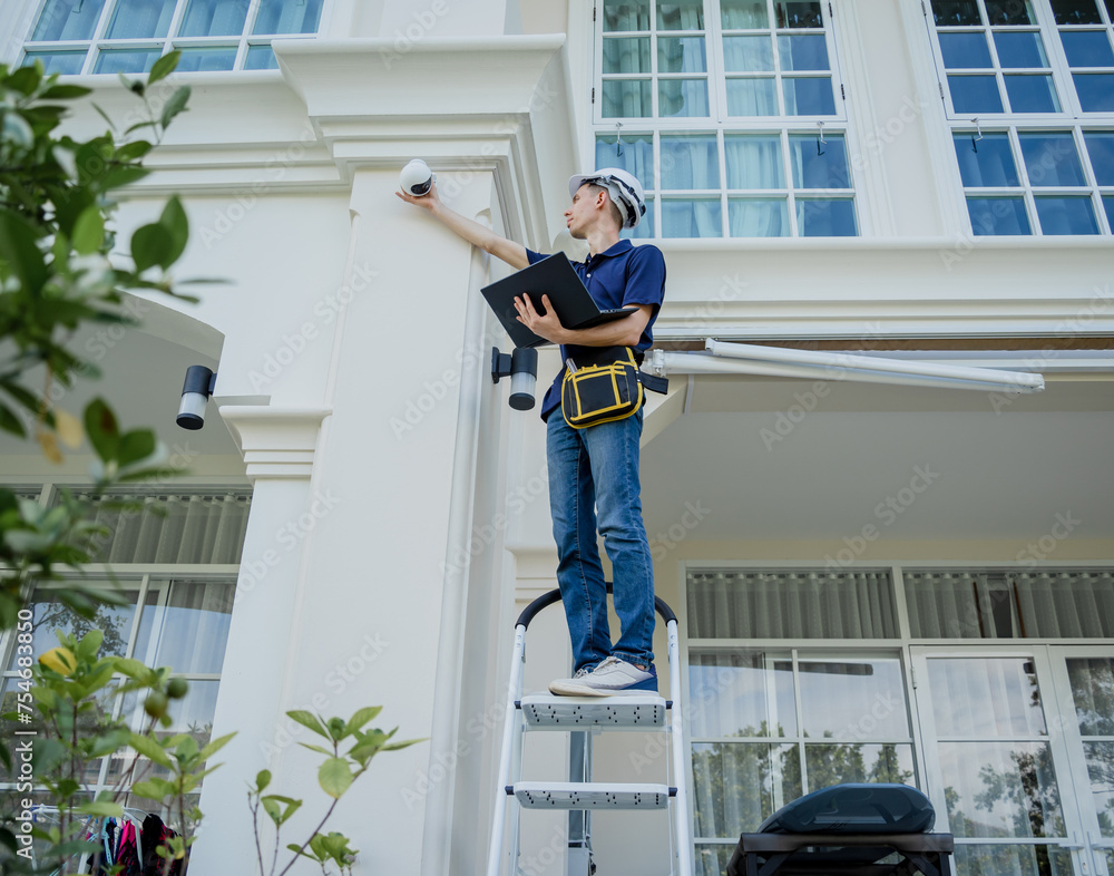 A technician sets up a CCTV camera on the facade of a residential building.