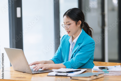 Asian businesswoman wear glasses working on digital laptop computer at table office. Technology and digital marketing online concept.