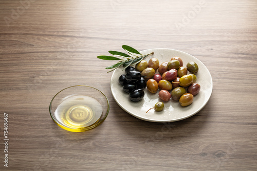 Olives with bunch of leaves in a white plate and olive oil on wooden background