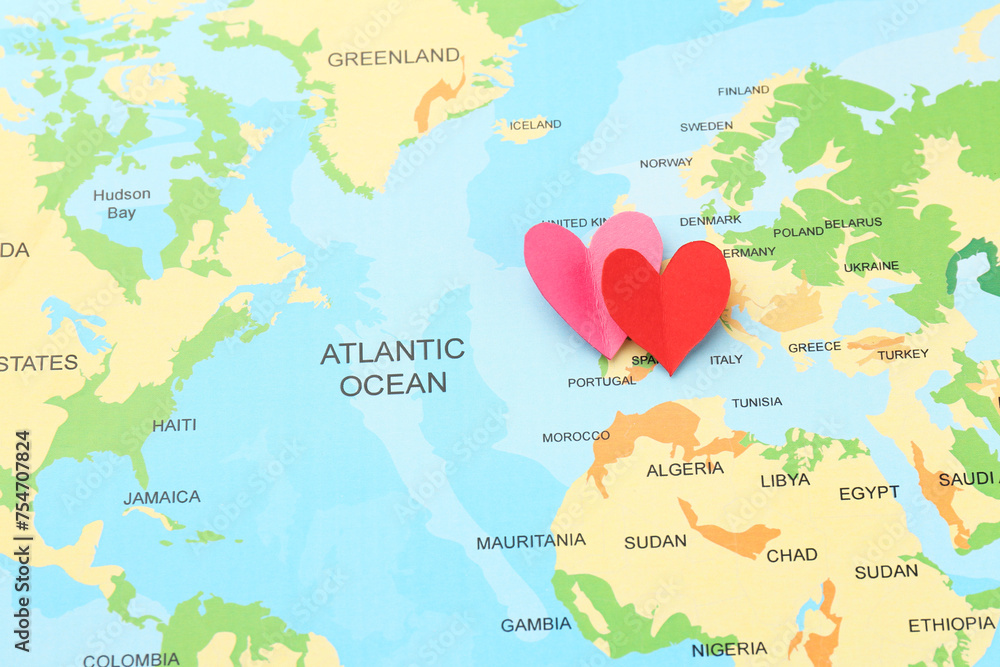 Fototapeta premium Honeymoon concept. Two red paper hearts on world map, top view