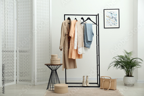 Rack with different stylish women's clothes, boots, bag and green houseplant indoors © New Africa