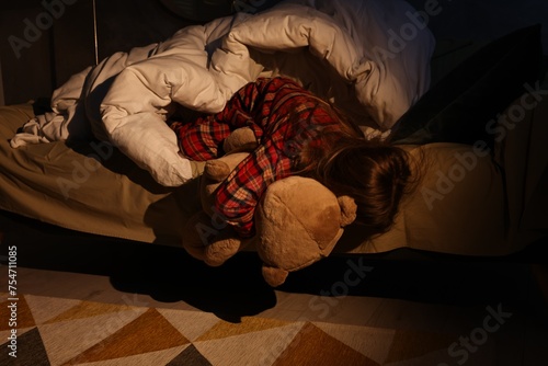 Little girl with toy looking for monster under bed at night