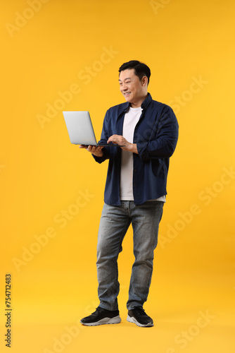 Full length portrait of happy man with laptop on yellow background